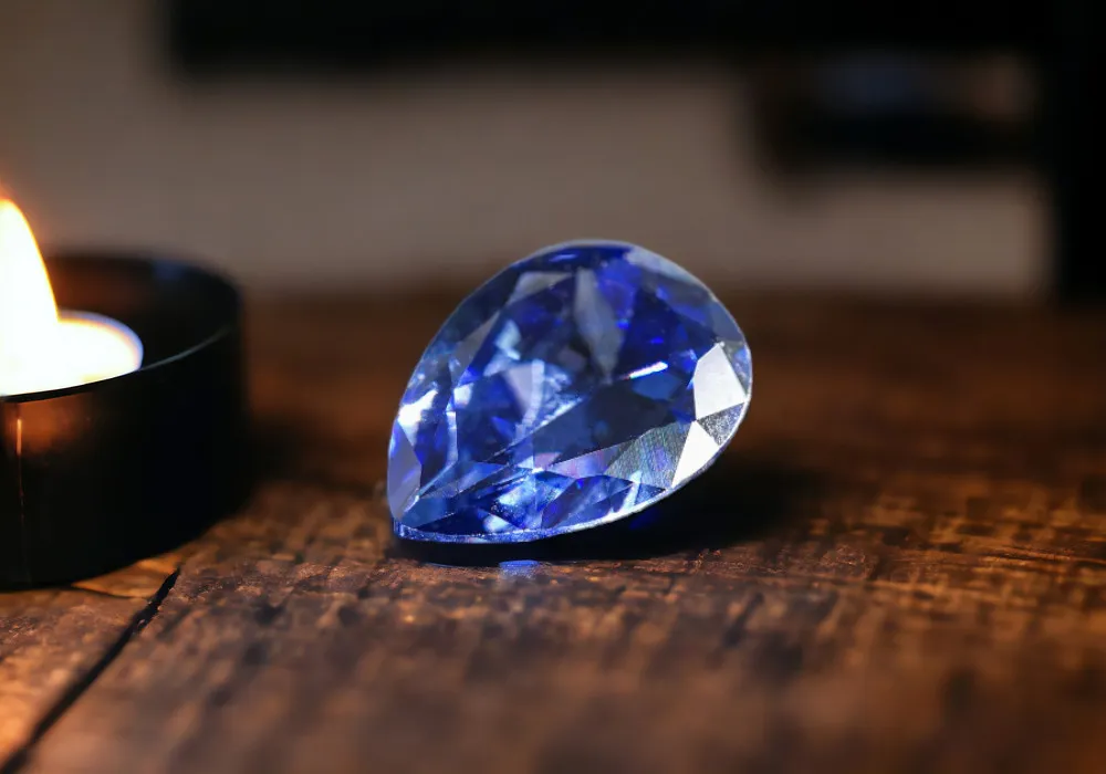 A Tanzanite stone sits on a wooden table next to a candle.