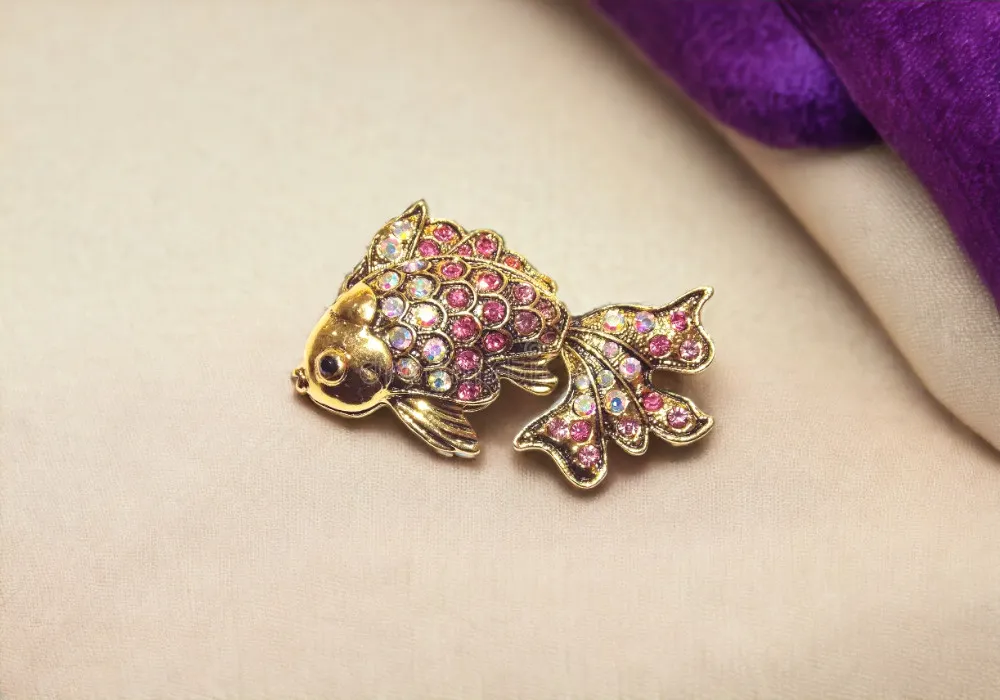 A gold and pink Fish Jewelry brooch with rhinestones.