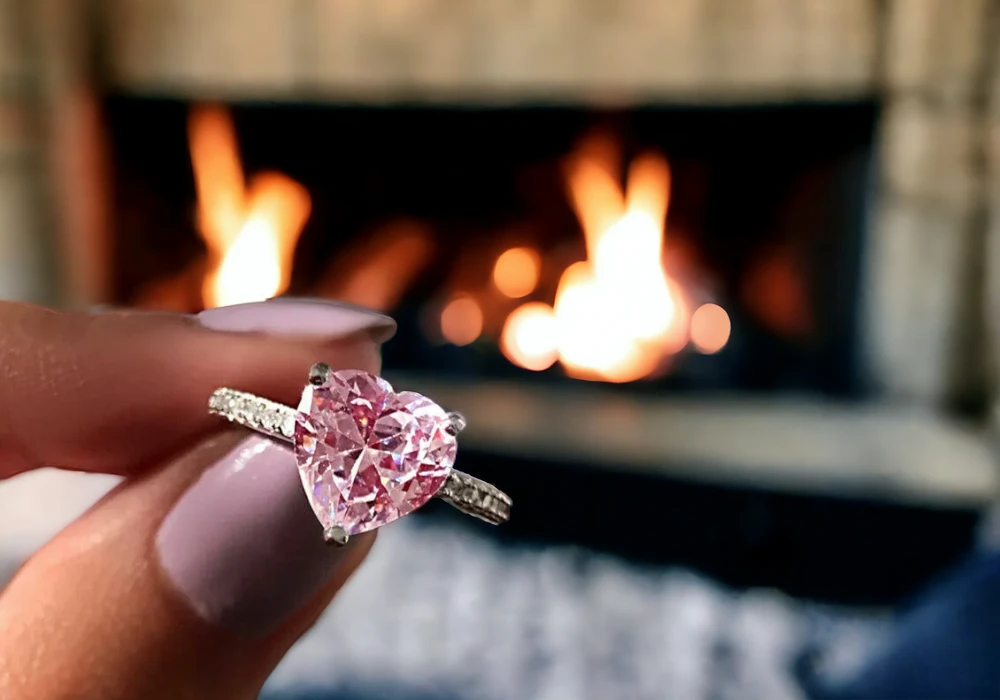 A hand holding a ring with a pink topaz gemstone in front of a fire.