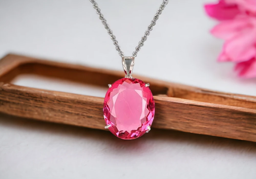 A pink gemstone pendant on a wooden board.