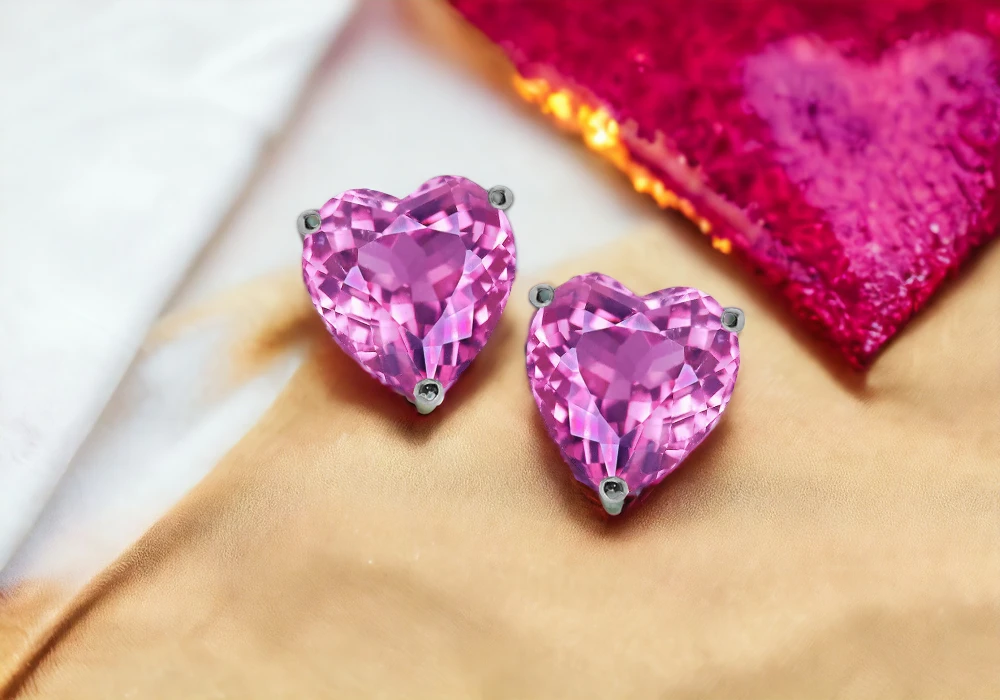 A pair of pink heart shaped stud earrings featuring pink gemstones.